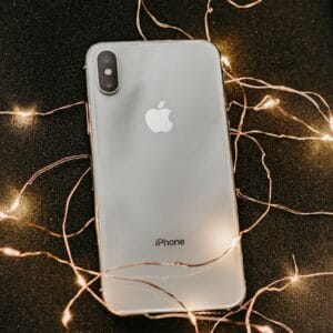 miglior iphone A sleek smartphone lies on a glittering black surface adorned with warm string lights, showcasing modern technology.